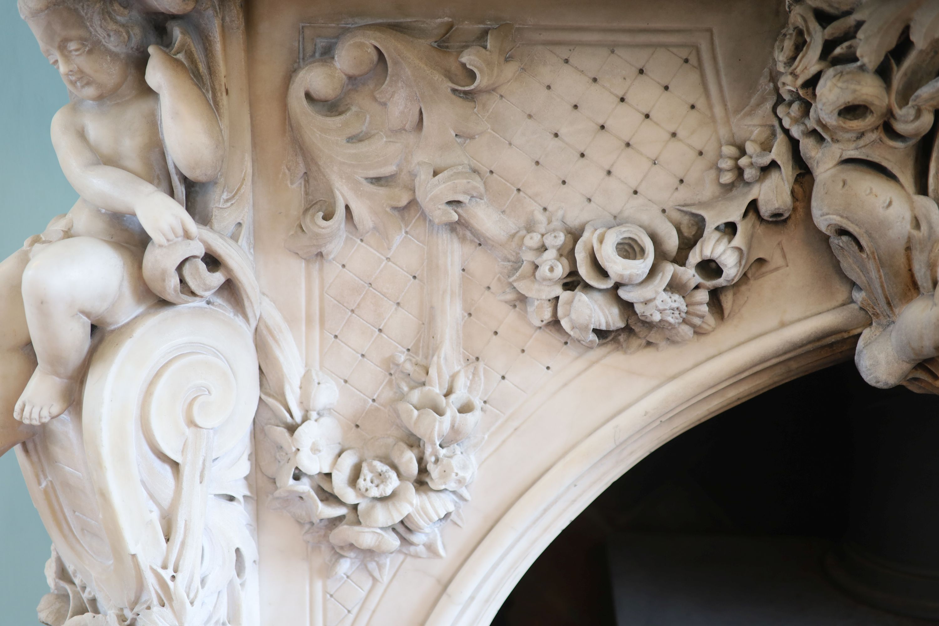 An important mid 19th century Italian white Carrara marble chimney piece, carved in the rococo taste, with seated putti, foliage swags